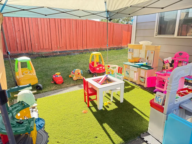 Shaded backyard play area with ride-on cars, a kids table and play kitchen