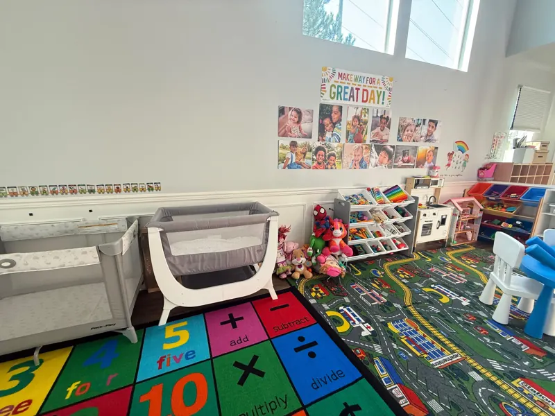 Bright classroom with a “Make way for a great day” wall, cribs and colourful learning rugs