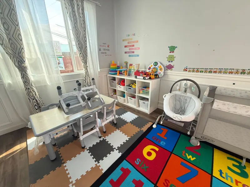 Infant and toddler room with a kids table, baby bouncer and numbers rug