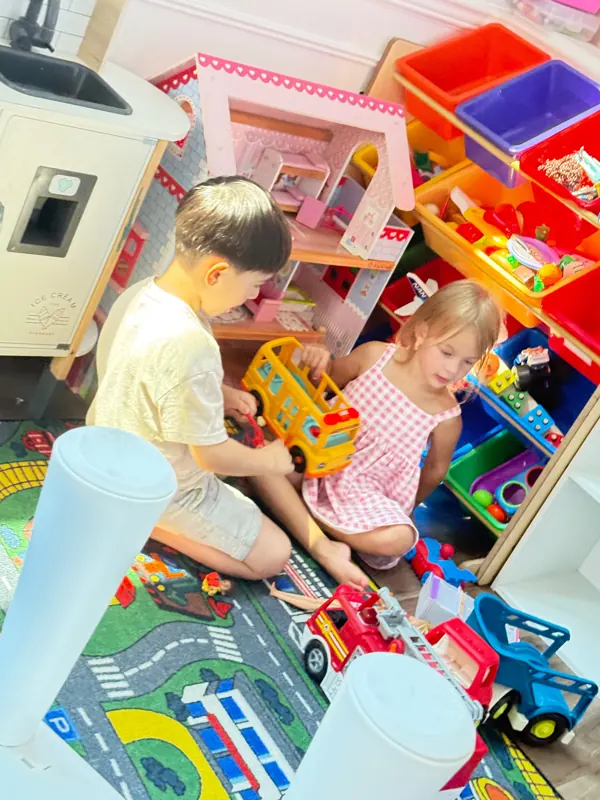 Two children playing together with toy cars and a dollhouse