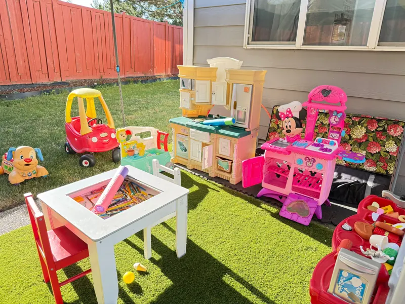 Outdoor play space on soft turf with a pretend kitchen and toy cars