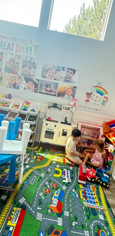 Children playing on a city-map rug under big sunny windows
